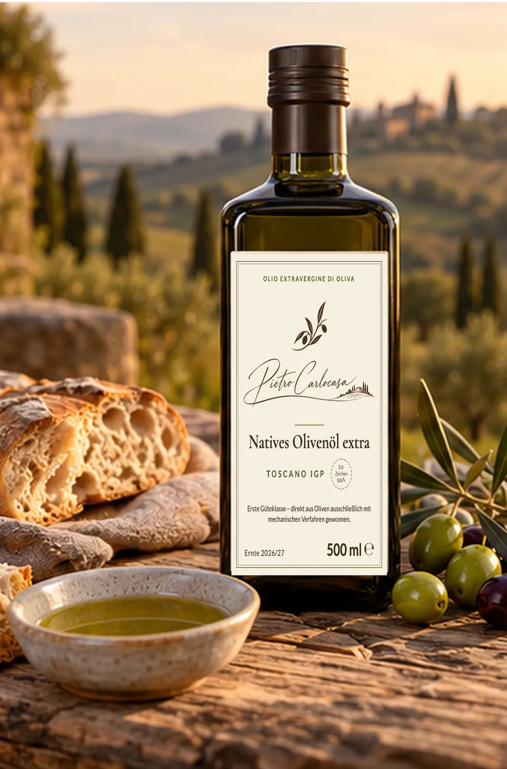Flasche Pietro Carlocasa Olivenöl vor toskanischer Hügellandschaft, daneben Brot, Oliven und eine Schale Öl